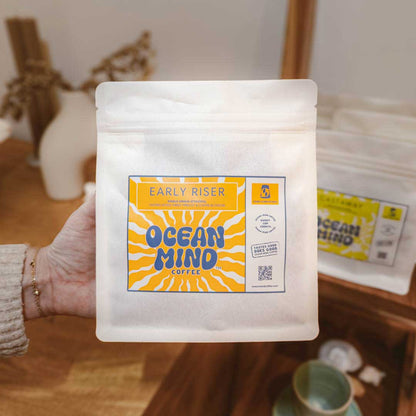 Hand holding a package of Early Riser Ocean Mind Coffee with an orange label