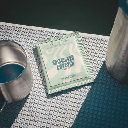 Sea Dog Ocean Mind Coffee steeped bag on a textured surface with a cup and container.